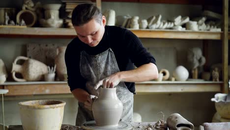 Experienced-ceramist-is-forming-ceramic-vase-from-clay-on-spinning-throwing-wheel-while-working-in-potter's-workshop.-Professional-is-focused-on-work.