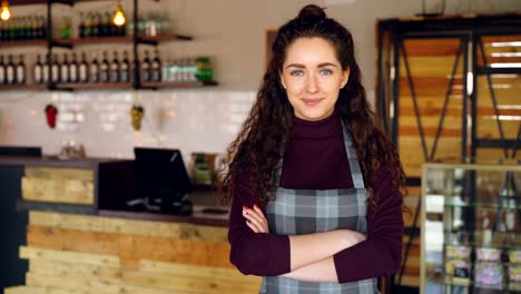 Retrato-de-mujer-atractiva-seguro-de-pequeño-empresario-en-su-apertura-de-cafetería-y-sonriente-mirando-a-cámara.-Interior-del-café-en-el-fondo.