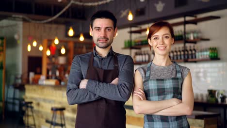 Retrato-de-dos-camareros-alegres-en-el-acogedor-café,-sonriendo-y-mirando-a-cámara.-Negocios-exitosos,-gente-atractiva-alegre-y-concepto-de-servicio-de-alimentos.