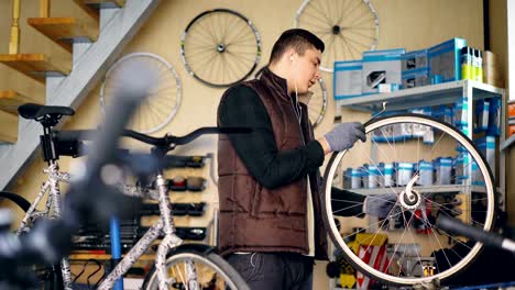 Selbstständige-Mechaniker-ist-Fahrrad-Rad-mit-Schraubenschlüssel-professionelle-Instrumente-reparieren,-während-der-Arbeit-in-kleinen-Werkstatt.-Junger-Mann-hört-Musik-mit-Kopfhörern.