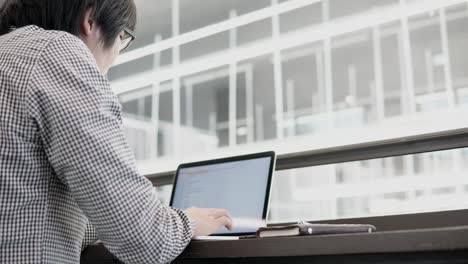 Hombre-de-negocios-asiático-joven-usando-la-computadora-portátil-en-el-espacio-de-trabajo-con-el-smartphone-y-el-portátil-en-el-escritorio-de-madera.-Macho-mano-escribiendo-en-el-teclado-del-ordenador-portátil.-Estilo-de-vida-independiente-en-concepto-