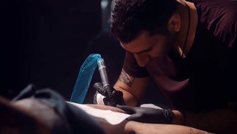 Professional-tattooist-using-tattoo-machine-and-working-on-client's-tattoo