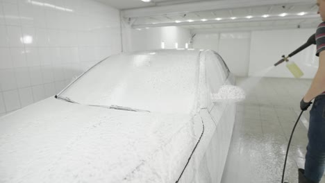 Man-sprinkling-with-foam-car-in-white-tiled-room