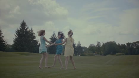 Three-girlfriends-round-dance-in-summer-field