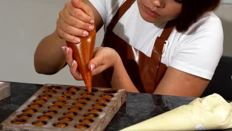 Junge-weibliche-chocolatier-Hinzufügen-von-Füllung-in-Schokoladenformen