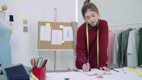 Young-Asian-woman-fashion-designer-drawing-using-pencil-and-looking-at-paper-while-working-in-the-workshop-studio.