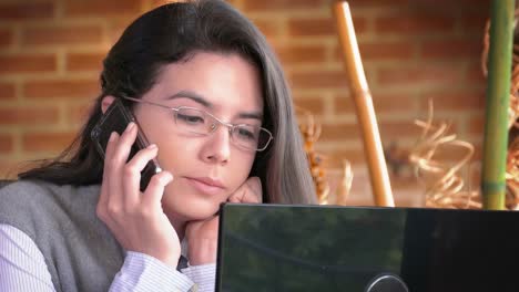 Home-Office.-Close-up-Dolly-Aufnahme-einer-freiberuflichen-Hispanic-junge-Frau-mit-Smartphone-und-Computer-Bildschirm-zu-lesen