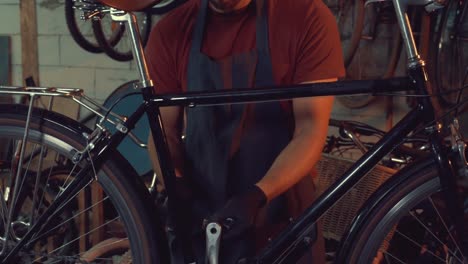 theme-small-business-bike-repair.-A-young-Caucasian-brunette-man-wearing-safety-goggles,-gloves-and-an-apron-uses-a-hand-tool-to-repair-and-adjust-the-bike-in-the-workshop-garage