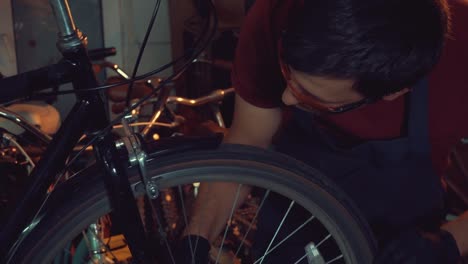 theme-small-business-bike-repair.-A-young-Caucasian-brunette-man-wearing-safety-goggles,-gloves-and-an-apron-uses-a-hand-tool-to-repair-and-adjust-the-bike-in-the-workshop-garage