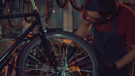 theme-small-business-bike-repair.-A-young-Caucasian-brunette-man-wearing-safety-goggles,-gloves-and-an-apron-uses-a-hand-tool-to-repair-and-adjust-the-bike-in-the-workshop-garage