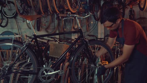 theme-small-business-bike-repair.-A-young-Caucasian-brunette-man-wearing-safety-goggles,-gloves-and-an-apron-uses-a-hand-tool-to-repair-and-adjust-the-bike-in-the-workshop-garage