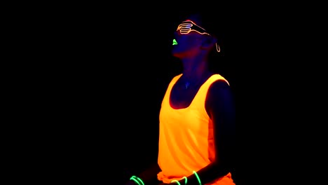 Woman-with-UV-face-paint,-glowing-clothing,-glowing-glasses,-bracelet-dancing-in-front-of-camera,-half-body-shot.-Asian-woman.-.