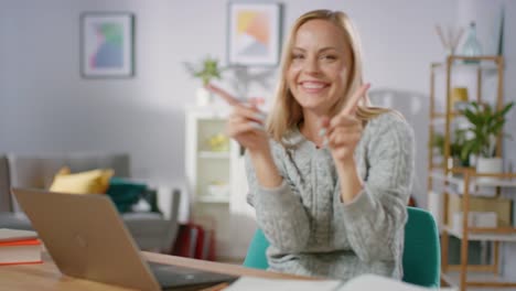 Hermosa-alegre-rubia-hace-divertido-baile-rutina-mientras-está-sentado-en-su-escritorio-en-la-sala-de-estar.-Mujer-feliz-haciendo-baile-celebratorio.