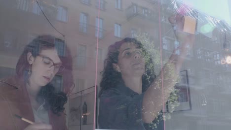 Two-businesswomen-brainstorm-on-windows-wall-over-real-estate