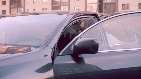 Young-woman-driver-open-door-of-car-and-sitting-into-car-on-parking-lot-in-city