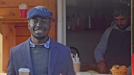 Smiling-man-standing-with-coffee-near-street-cafe