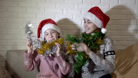 Alegres,-felizes-niñas-sombrero-rojo-de-Santa-Claus-juego-con-otros-espumillones,-reír-y-sonrían-sentado-en-el-sofá-contra-la-pared-de-ladrillo-blanco.