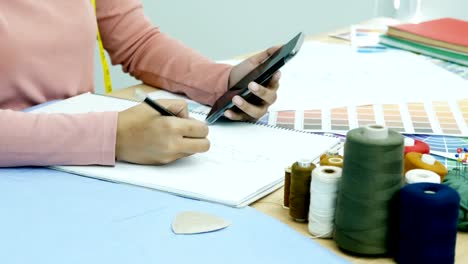 Cerca-mano-de-fabricante-Vestido-de-dibujo-para-el-diseño-del-vestido-sobre-el-papel.-Vestido-a-fabricante-utilizando-smartphone-para-encontrar-la-inspiración-con-su-diseño.