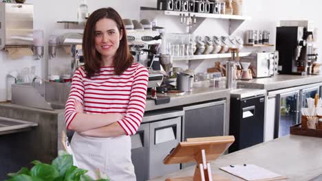 Young-female-coffee-shop-owner-crossing-arms-behind-counter