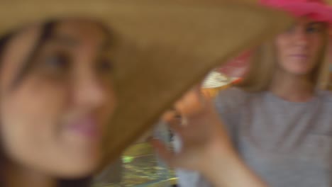 Acercamiento-de-dos-mujeres-jóvenes-tratando-en-sombreros-en-una-tienda