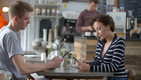 Adult-couple-sitting-in-a-cafe-using-smartphones,-close-up