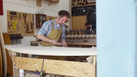 Man-Shaping-Custom-Surfboard-en-el-taller-filmado-en-la-cámara-roja