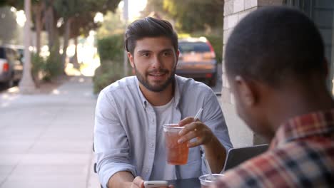 Dos-amigos-masculinos-adultos-hablando-sobre-refrescos-fuera-de-café