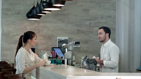 Sonriendo-barista-y-bonita-joven-hablando-en-cafetería