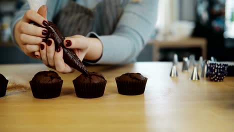 Nahaufnahme-der-weiblichen-Hände-legt-die-Creme-aus-Spritzbeutel-auf-Schokoladen-Cupcakes.-Junge-Frau,-die-kochen-die-muffins