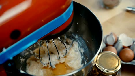 Vista-de-primer-plano-de-manos-femeninas-agrega-el-huevo-y-se-convierte-en-el-mezclador.-Mujer-cocina-la-pasta-en-el-recipiente-en-la-cocina