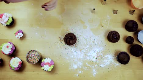 Top-view-of-young-female-hands-decorating-the-chocolate-cupcake-or-muffin-with-cream,-using-pastry-bag-for-this