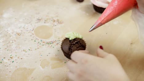 Close-up-view-of-female-hands-decorating-the-chocolate-cupcake-with-colored-cream,-using-pastry-bag-for-this