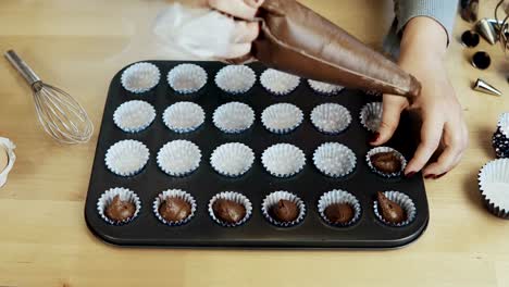 Nahaufnahme-von-weiblichen-Händen-den-Teig-in-die-Wrapper,-Pappbecher-für-Cupcakes,-mit-Spritzbeutel-setzen