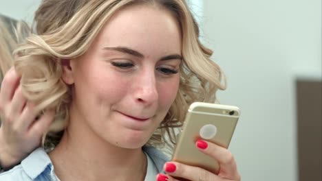 Woman-having-hair-styling-in-salon-while-browsing-the-internet-on-her-mobile-phone,-smiling