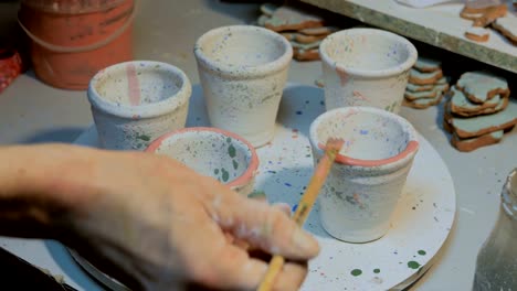 Professional-male-potter-painting-mugs-in-pottery-workshop