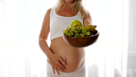 smiling-woman-with-naked-abdomen-keeps-dish-with-fresh-fruits-and-look-in-camera