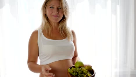 mujer-con-bebé-en-el-vientre-tiene-frutas-en-el-plato-y-come-las-uvas-junto-a-la-ventana,-sanos-comer