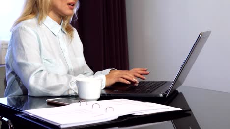 Una-mujer-lee-documentos-importantes-en-una-carpeta-y-tipos-en-un-ordenador-portátil