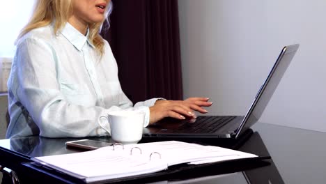 A-woman-reads-important-documents-in-a-folder-and-types-it-into-a-laptop