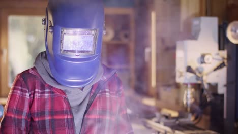 Young-attractive-woman-welds-metal-in-a-workshop-and-reveals-her-beautiful-face