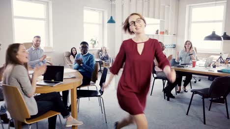 Camera-follows-European-female-boss-exiting-multi-ethnic-modern-office,-doing-crazy-dance-walk-of-success-and-victory-4K