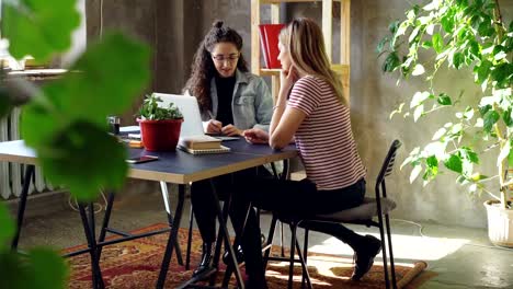 Jóvenes-emprendedores-son-estrategias-de-publicidad-de-duscussing-sentado-a-la-mesa-en-la-oficina-moderna.-Las-mujeres-están-hablando-y-gesticulando,-uno-de-ellos-está-haciendo-notas.