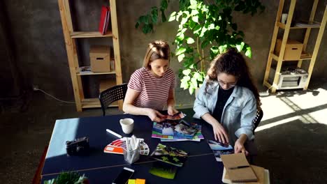 Erhöhte-Ansicht-junger-Designer-stellen-Fotos-an-Tisch-perfekt-flach-Laien-arbeiten-im-Studio-zu-erstellen.-Sie-sitzen-am-Tisch-zusammen-und-diskutieren-verschiedene-Fotos