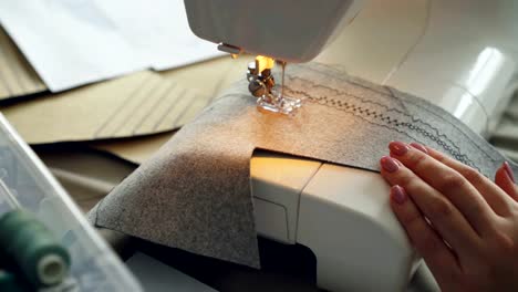 Close-up-shot-of-working-sewing-machine,-fabric-and-manicured-female-hand.-Clothes-manufacturing-process-concept.-Light-soft-colours