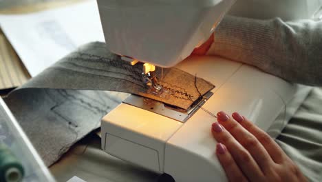 Close-up-view-of-modern-electric-sewing-machine-working-stitching-piece-of-fabric.-Girl's-manicured-hand-and-colorful-sewing-threads-are-visible.