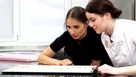 Two-female-confectioners-examining-meringues-on-a-tray