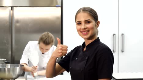 Happy-female-chef-smiling-showing-thumbs-up-at-the-kitchen