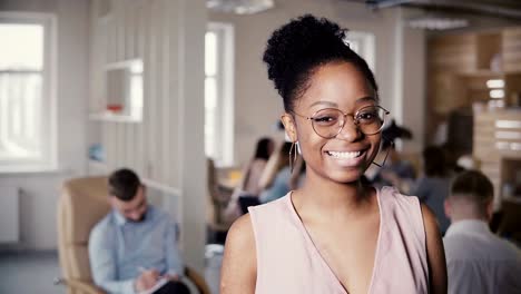 Porträt-von-schönen-jungen-afroamerikanischen-erfolgreiche-Geschäftsfrau,-Blick-in-die-Kamera-im-Loft-Büro-Hintergrund-4K