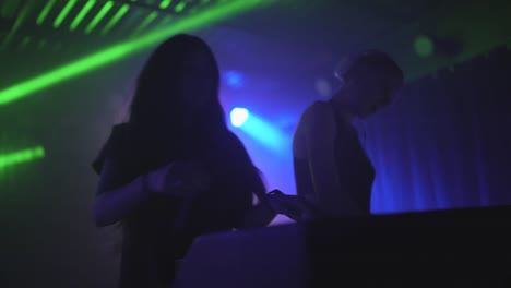 Dos-hermosas-mujeres-jóvenes-DJ-juegan-la-música-en-la-mesa-de-mezclas-en-la-discoteca