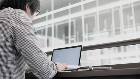 Young-Asian-business-man-using-laptop-computer-in-working-space-with-smartphone-and-notebook-on-wooden-desk.-Male-hand-typing-on-laptop-keyboard.-Freelance-lifestyle-in-digital-age-concept.